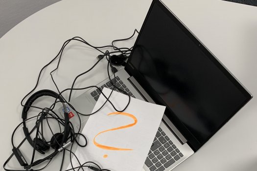 Laptop mit diversen Kabeln und einem Kopfhörer, darauf liegt ein Zettel mit einem großen Fragezeichen